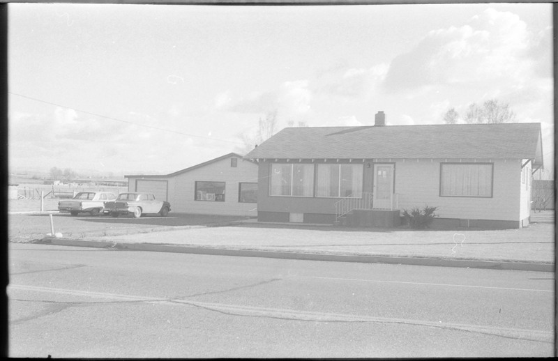 A photograph of a home and outbuilding. The outbuilding has two cars parked in front and an "Open" sign is visible in the window.