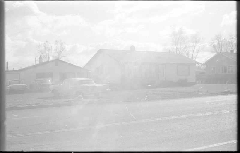 A photograph of a home and outbuilding. The outbuilding has three cars parked in front.