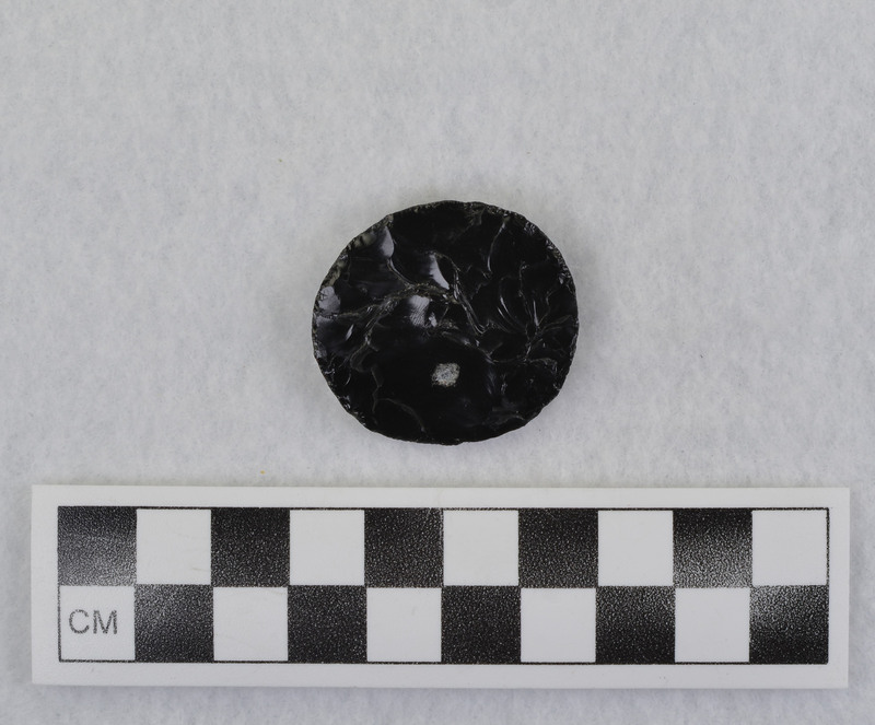 Spheroid/plano-convex indentation on plano side, "Due to pecking from tool engraver (electric). Crabtree was probably going to perforate this to be used as a pendant. See Crabtree 1472, pg 31 (cone principal paper). (JW) Tebiwa, Vol. 15, No. 2, 1972, pp. 29-42."