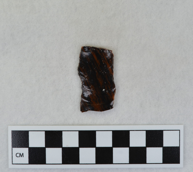 A channel flake, proximal end, from a Clovis point created by Donald E. Crabtree. This object mends with seven other objects in the collection; Ce.3845 - Ce.3852. The object was made using percussion fluting with a hammerstone while the distal end rested on an anvil. Ce.3847, Ce.3848, and Ce.3849 make up the channel flake from the labeled side of the object.