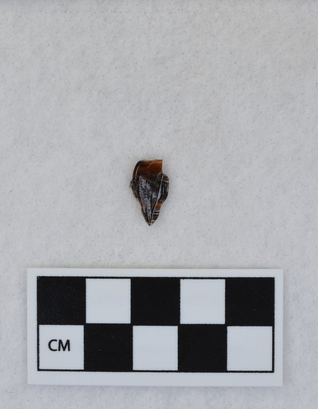 A channel flake, distal end, from a Clovis point created by Donald E. Crabtree. This object mends with seven other objects in the collection; Ce.3845 - Ce.3852. The object was made using percussion fluting with a hammerstone while the distal end rested on an anvil. Ce.3847, Ce.3848, and Ce.3849 make up the channel flake from the labeled side of the object.