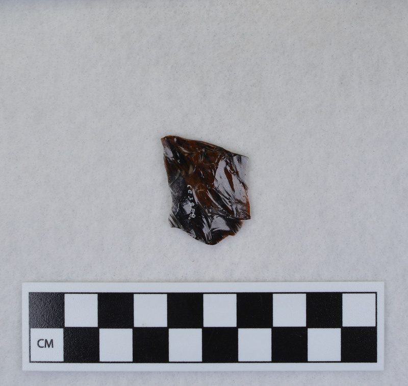 A channel flake, proximal end, from a Clovis point created by Donald E. Crabtree. This object mends with seven other objects in the collection; Ce.3845 - Ce.3852. The object was made using percussion fluting with a hammerstone while the distal end rested on an anvil. Ce.3850, Ce.3851, and Ce.3852 make up the channel flake from the unlabeled side of the object.