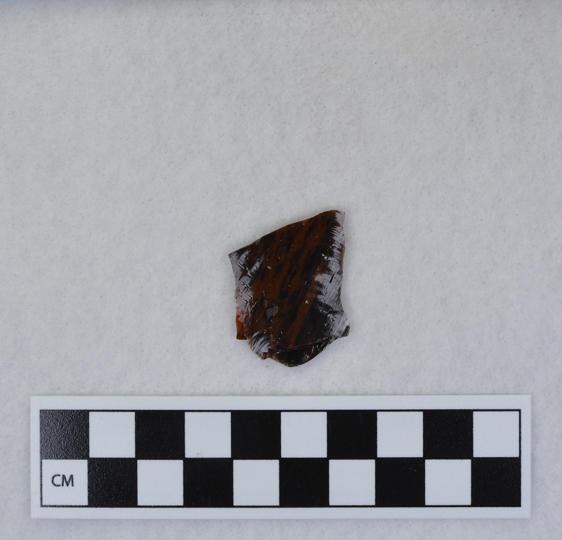 A channel flake, proximal end, from a Clovis point created by Donald E. Crabtree. This object mends with seven other objects in the collection; Ce.3845 - Ce.3852. The object was made using percussion fluting with a hammerstone while the distal end rested on an anvil. Ce.3850, Ce.3851, and Ce.3852 make up the channel flake from the unlabeled side of the object.