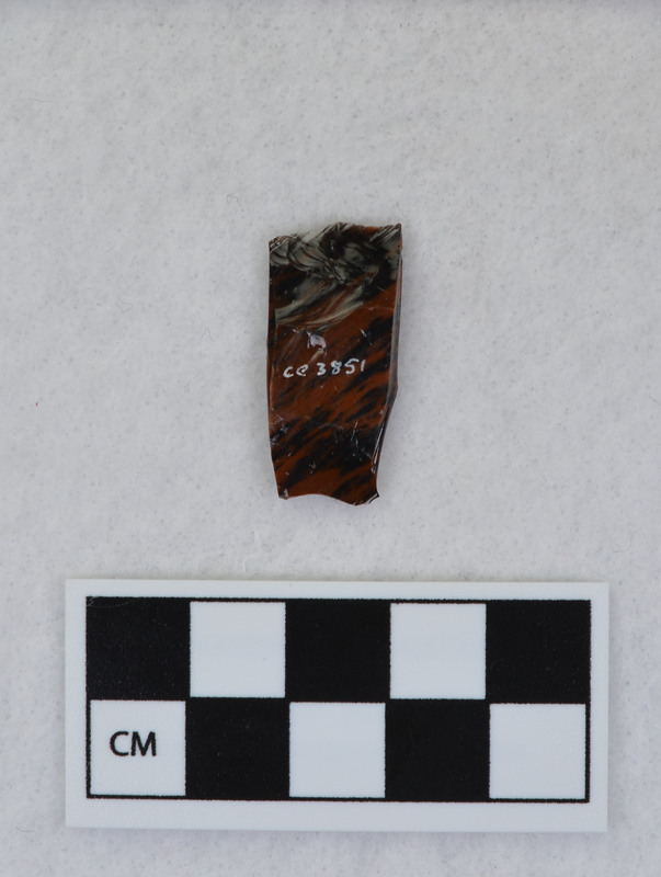A channel flake, medial section, from a Clovis point created by Donald E. Crabtree. This object mends with seven other objects in the collection; Ce.3845 - Ce.3852. The object was made using percussion fluting with a hammerstone while the distal end rested on an anvil. Ce.3850, Ce.3851, and Ce.3852 make up the channel flake from the unlabeled side of the object.