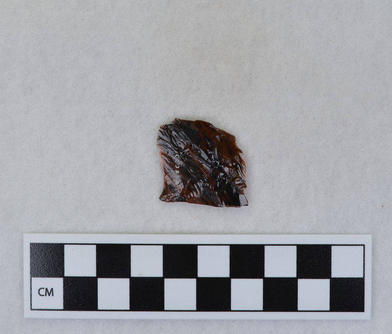 A channel flake, distal end, from a Clovis point created by Donald E. Crabtree. This object mends with seven other objects in the collection; Ce.3845 - Ce.3852. The object was made using percussion fluting with a hammerstone while the distal end rested on an anvil. Ce.3850, Ce.3851, and Ce.3852 make up the channel flake from the unlabeled side of the object.