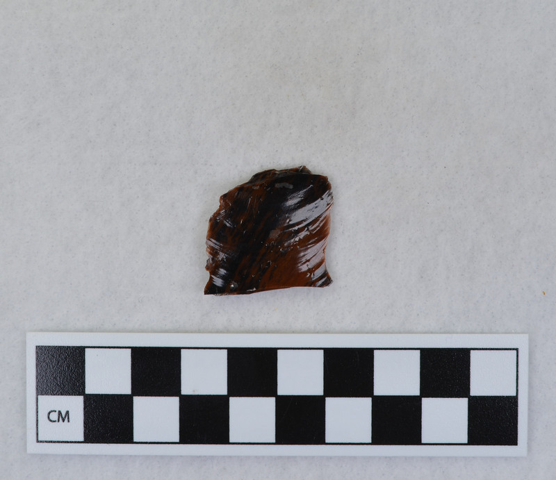 A channel flake, distal end, from a Clovis point created by Donald E. Crabtree. This object mends with seven other objects in the collection; Ce.3845 - Ce.3852. The object was made using percussion fluting with a hammerstone while the distal end rested on an anvil. Ce.3850, Ce.3851, and Ce.3852 make up the channel flake from the unlabeled side of the object.