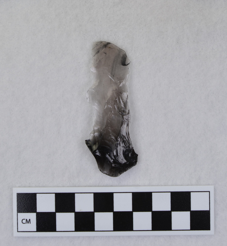 A fluting error from Donald E. Crabtree's early fluting experiments. This is a channel flake connected to the distal end of Clovis point. The Clovis point was ground and rested on anvil. The channel flake and tip were removed when too much downward motion was initiated while attempting to flute the point. (JW) Mends with Ce.1067 and Ce.1068.