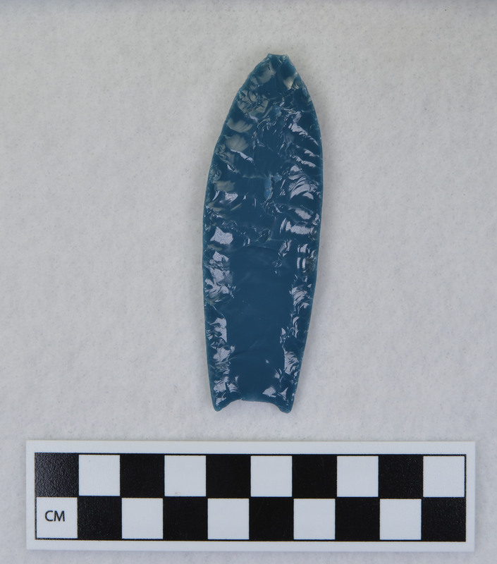 A Folsom point created by Donald E. Crabtree during his Folsom experiments. Created from light blue art glass, this point is lightly ground on the channel flake platforms.