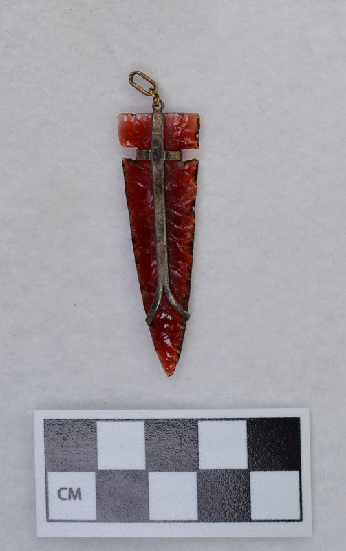 Donald E. Crabtree made this side notched biface out of red glass. He mounted the biface for a necklace.