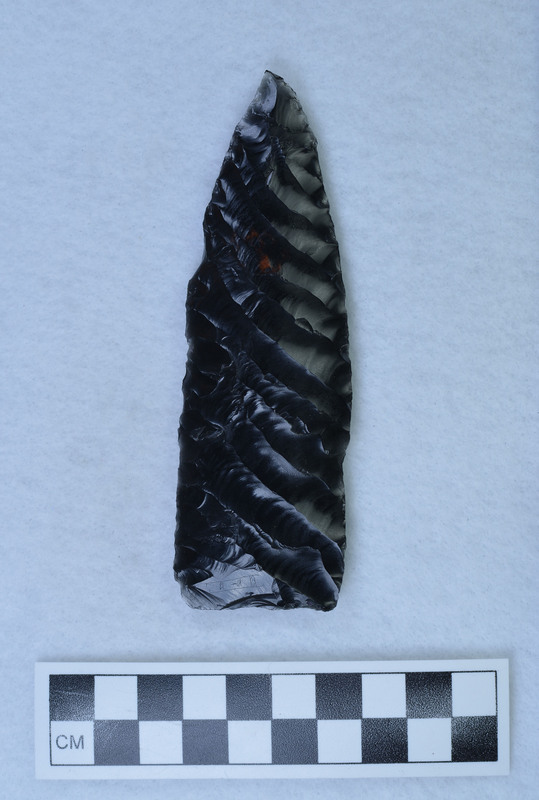 An unfinished obsidian biface created by Donald E. Crabtree. The completed side has flakes running margin to margin, with one flake exceeding the margin (outrepasse in French). The object is also signed by Crabtree. On the unfinished side "percussion" is etched. (JW)
