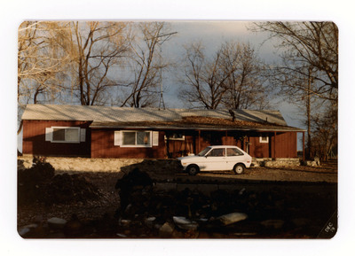 The front of a postcard decorated with a picture of a car parked in front of a house.