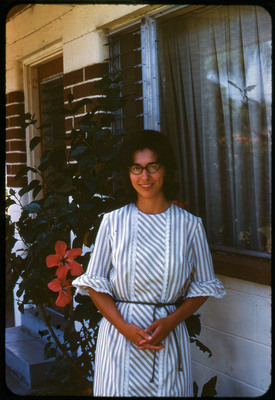 A photographic slide of a woman smiling in front of a house