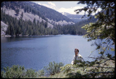 A photographic slide of Evelyn Crabtree standing behind a tree in front of a body of water.