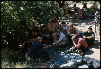 A photographic slide of a group of people huddled together watching as a demonstration is being filmed.