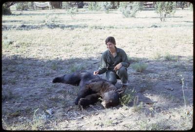 A photographic slide of a person sitting behind a dead bear.