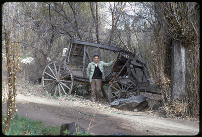 A photographic slide of a man posing next to a dilapidated carriage.