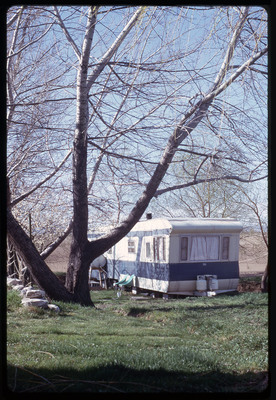 A photographic slide of an RV parked outside in the grass under a tree.