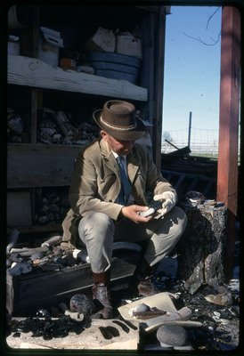 A photographic slide of a man with a pipe standing next to a cliffside.