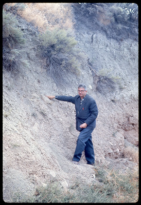 A photographic slide of a man with a pipe standing next to a cliffside.