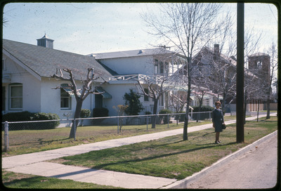 A photographic slide of a woman standing in front of a large white house.