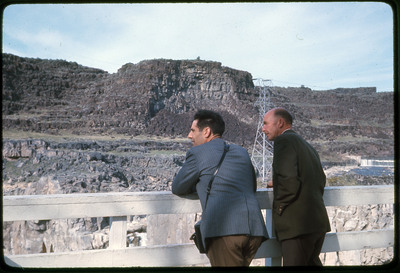 A photographic slide of two men looking over a tall cliffside.