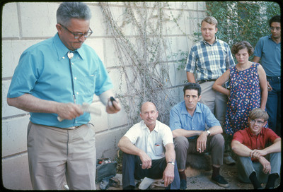 A photographic slide of A group of people, including Don E. Crabtree, gathered watching Francois Bordes flintknap.
