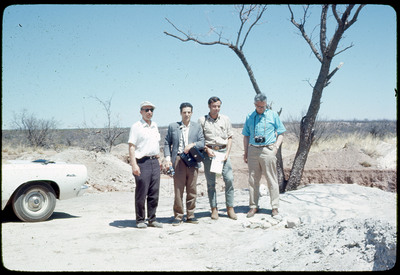 A photographic slide of four men standing together in a desert.