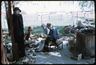A photographic slide of three men flintknapping on a porch while a fourth man watches.
