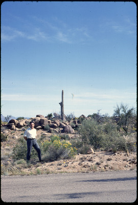 A photographic slide of a man posing in front of a tall cactus surrounded by rocks.
