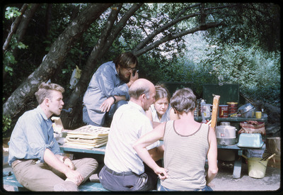 A photographic slide of a group of people gathered on a park bench over an unknown item.