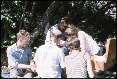 A photographic slide of a group of people gathered on a park bench over an unknown item.