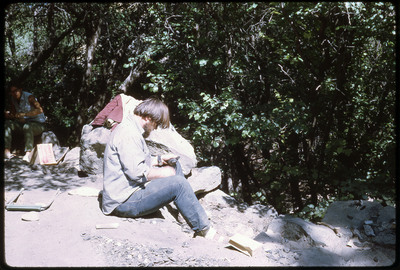 A photographic slide of a man flintknapping outside.