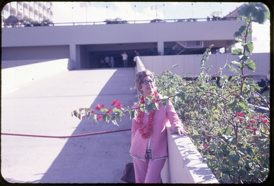 A photographic slide of Evelyn Crabtree wearing a floral lei necklace posing behind tropical flowers.