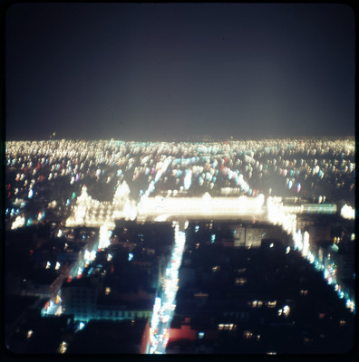 A photographic slide displaying an aerial view of a cityscape at night. Bright, blurry, yellow lights dot the scene.