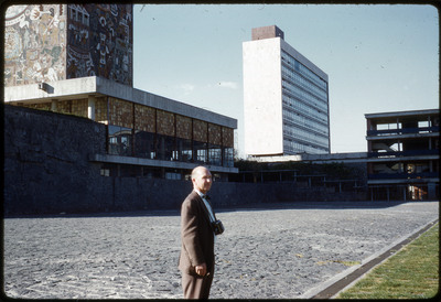 A photographic slide of Don E. Crabtree standing in front of a building decorated with historical art.