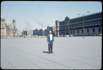 A photographic slide of Don E. Crabtree standing in a large urban area near a few historical buildings.