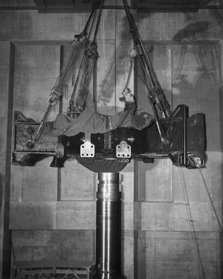 The spider for the L-7 generator, after being heated to cause it to expand, is being lowered onto its shaft. It is partially covered with canvas to keep it warm until it is in place.