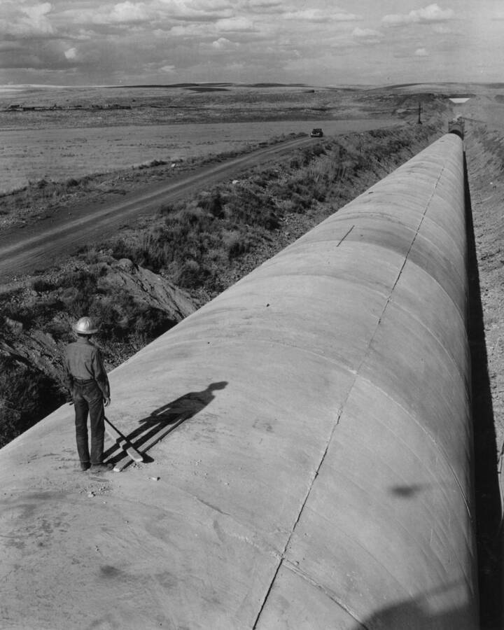 Columbia Basin Project, Irrigation Division, West Canal, Specifications No. 1286--Utah Construction Co. and Winston Bros. Co., Contractor. Looking easterly over completed portion of Dry Coulee Siphon No. 1 from Section 172. Steel yard, where siphon re-steel is cut, rolled, and welded is at left background. H.E. Foss, photographer.