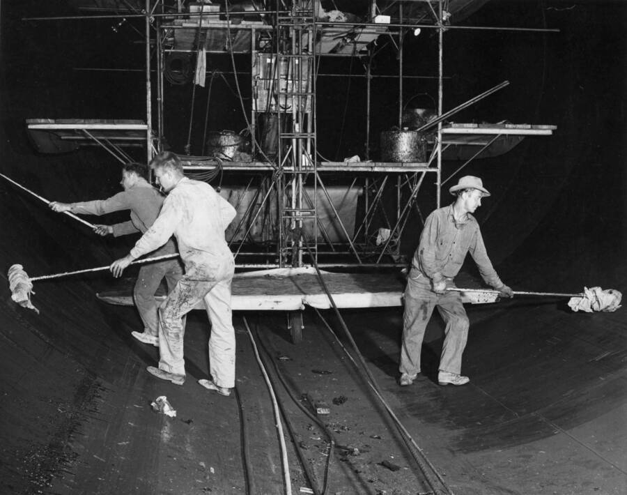 Columbia Basin Project, Irrigation Division, Soap Lake Siphon, Specifications 2411. Workmen removing dust from coal-tar primer prior to applying coal-tar enamel. Rags wrapped around sweep brooms are used. The enameling stage is in the background. This work is being performed by Walter Ferem Company, Los Angeles, sub-contractor for Winston-Utah under Schedule II of the above specifications. H.E. Foss, photographer.