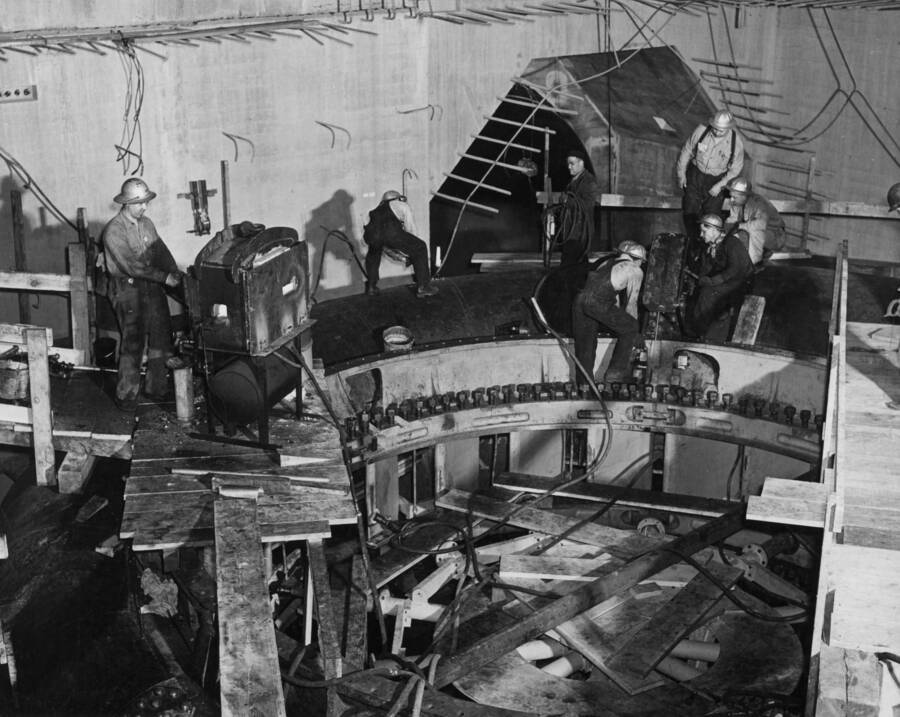 Riveting together the sections of the #1 Shasta turbine scroll case in pit 7. On the left is the heater. In the center, a man is bouncing a heated rivet to knock off the oxidized scale and on the right are the riveters waiting for the rivet.