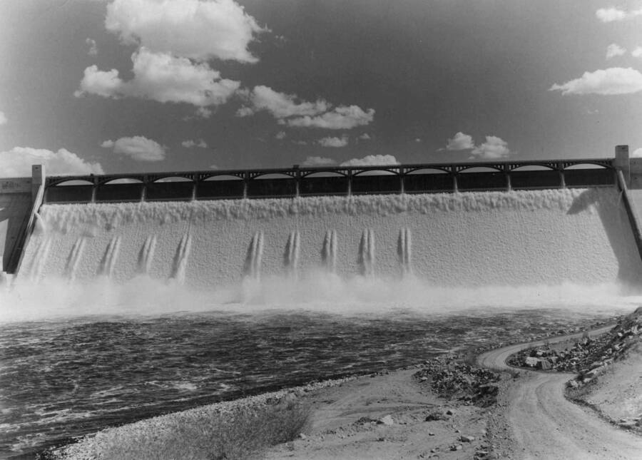 General view of the spillway section of Grand Coulee Dam, taken from the west bank for the Columbia River. On this date, approximately 80,000 cubic feet of water per second was plunged nearly 350 feet vertically down the face of the dam, creating a waterfall more than twice the height of Niagara. An additional 25,000 cubic feet of water per second is passing through the hydro-turbine installed in the west powerhouse.
