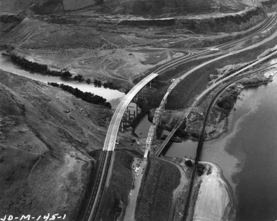 A few miles above the south shore axis of the U.S. Army Corps of Engineers John Day Lock and Dam on the Columbia River, the newly relocated Interstate Highway 80N and the Union Pacific transcontinental main line swing across the John Day River. Here is shown the new four lane highway bridge at John Day and the new Union Pacific Bridge necessitated by the relocation work. Riverward from the two new crossings may be seen the old highway bridge and the Union Pacific bridge as they cross the John Day River at the present Columbia River level. Both of these approaches will be inundated with the creation of the John Day reservoir.