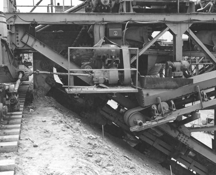 Columbia Basin Project, Irrigation Division, 2nd Section West Canal, Specs. 2541. Close-up showing drive mechanism excavating buckets and conveyor belts on the right front side of the trimmer. Left side is similar. Work is being performed by Morrison-Knudsen, Inc. under Schedule 2 of above Specifications. H.E. Foss, photographer.