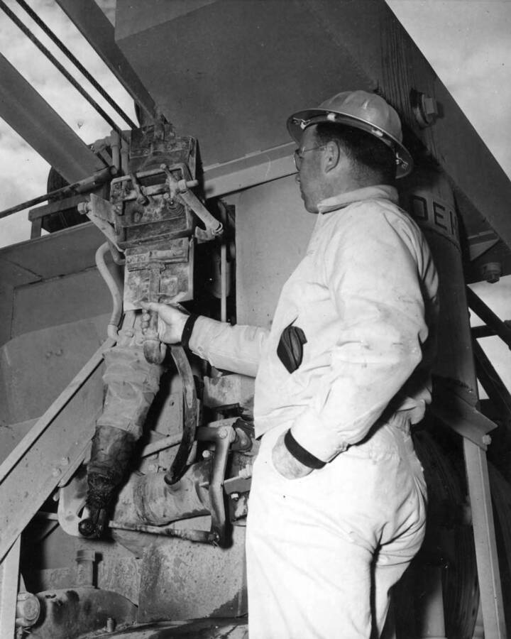 Columbia Basin Project, Irrigation Division, 2nd section West Canal, Specs. 2541. Job-made A.E.A. dispenser on one of the Koehring 34E concrete mixers being examined by Chief Inspector Lloyd C. Russell. It is the rubber bag type, actuated by the charging skip. Work is being performed by Morrison-Knudsen, Inc. under Schedule 2 of above specifications. H.E. Foss, photographer