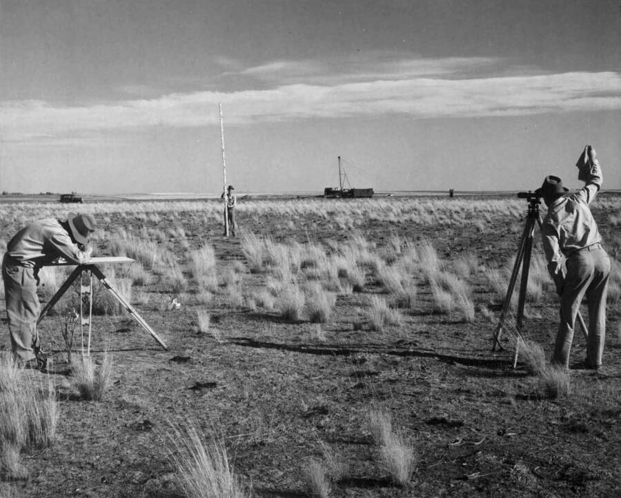 Columbia Basin Project, Irrigation Division. Predevelopment Farm No. 1; located approx. 2 miles east of Moses Lake, Wash. Crew of Agricultural engineers taking topography in view of land leveling and laying out of irrigation distribution system. Farm covers 80 acres. Water supply well may be seen in distance, and the town of Wheeler may be seen in extreme left background. Men in picture are, left; M.W. Hoisveen, USBR Agriculture Eng.; center, B.W. Doran, USBR Agriculture Eng.; right, H.A. Sandwick, USBR Agriculture Eng. Photo taken for J.L. Toevs, chief of land development.