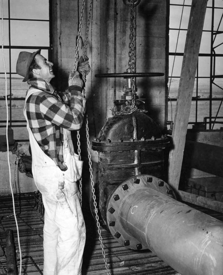 Setting one of three 16-inch gate valves on pump discharge pipes in the Burbank Pump Plant. This feature under construction about 7 miles east of Pascoe, Washington by Pfieffer and Hohner. Specifications R1-CB-16 H.E. Foss, photographer