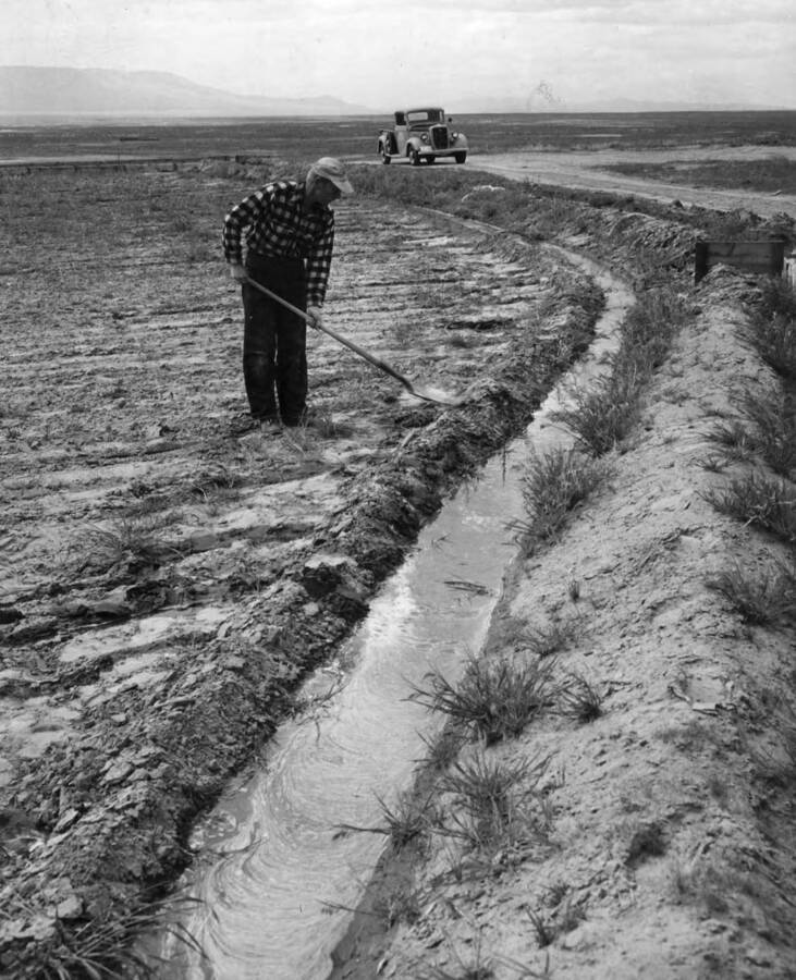 Columbia Basin Project, Irrigation Division, Pasco Settlers. Robert McNulty, Unit 1, whose farm is first on the lateral distribution system, works on a ditch around his fields. Much of his acreage is irrigated by a wooden flume, part of which may be seen at upper left. H. Foss, photographer