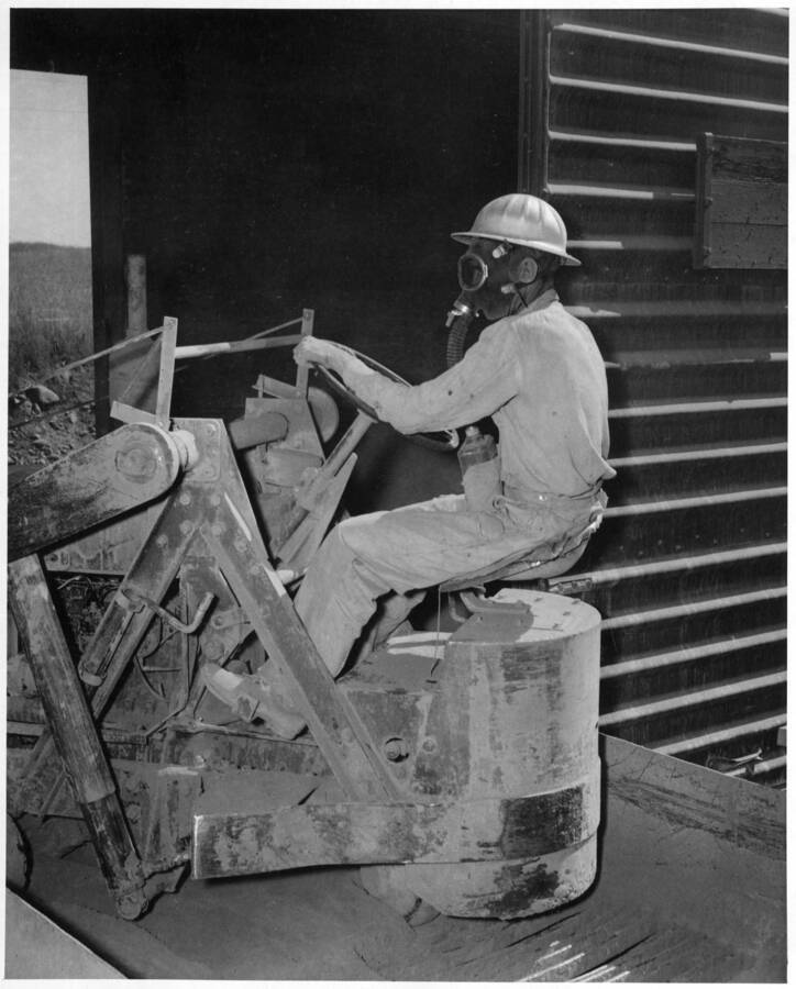 Columbia Basin Project--Irrigation Division. West Canal and East Low Canal--Specifications 1286 and 1422. Workman unloading bulk cement with Butler Car scoop. Job Hazards are minimized by the use of proper safety equipment. H.E. Foss, photographer.