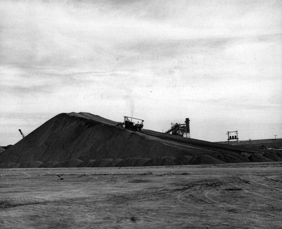 Columbia Basin Project, Irrigation Division, Specifications No. 2541, West Canal, Second Section. Contractor: Morrison-Knudsen Company, Inc. Bulldozer pushing material into final position in stockpile produced by M.E. Nelson Construction Company, subcontractor furnishing the gravel for concrete. This material will be rescreened by the subcontractor prior to batching. Note top of batching plant beyond the stockpile. H. E. Foss, photographer
