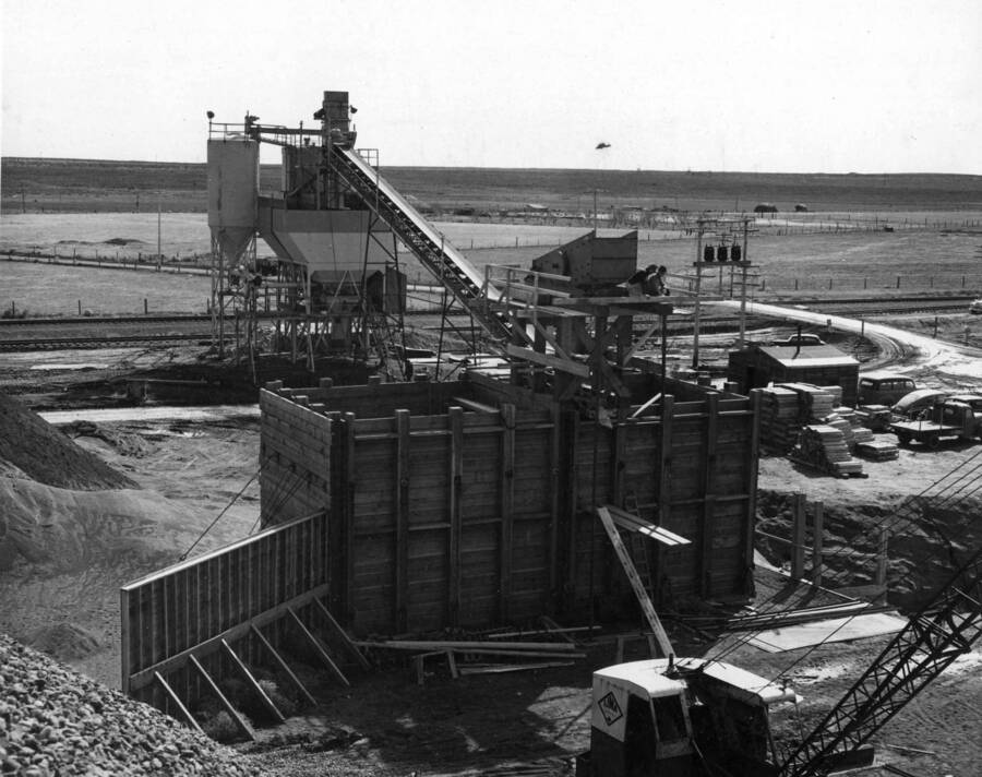 Columbia Basin Project, Irrigation Division, Specifications No. 2541, West Canal, Second Section. Contractor: Morrison-Knudsen Inc. View shows construction of bins and rescreening plant installed by subcontractor M.E. Nelson Construction Company with prime contractor's batching plant in the background. Materials rescreened are stored in the timber bins and fed through gates in the bottom onto conveyor belt in tunnel. Sloping sides have been constructed within the bins to eliminate dead storage space.